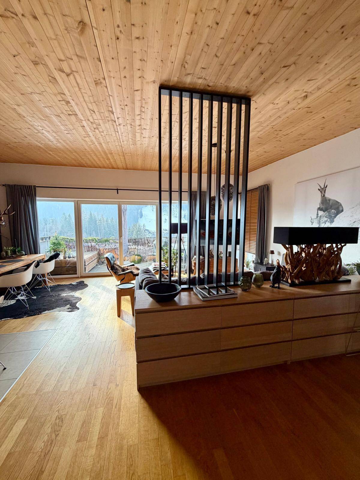 Heller Wohnbereich mit Holzbalkendecke, Parkettboden und Zugang zu einem Balkon oder einer Terrasse.
