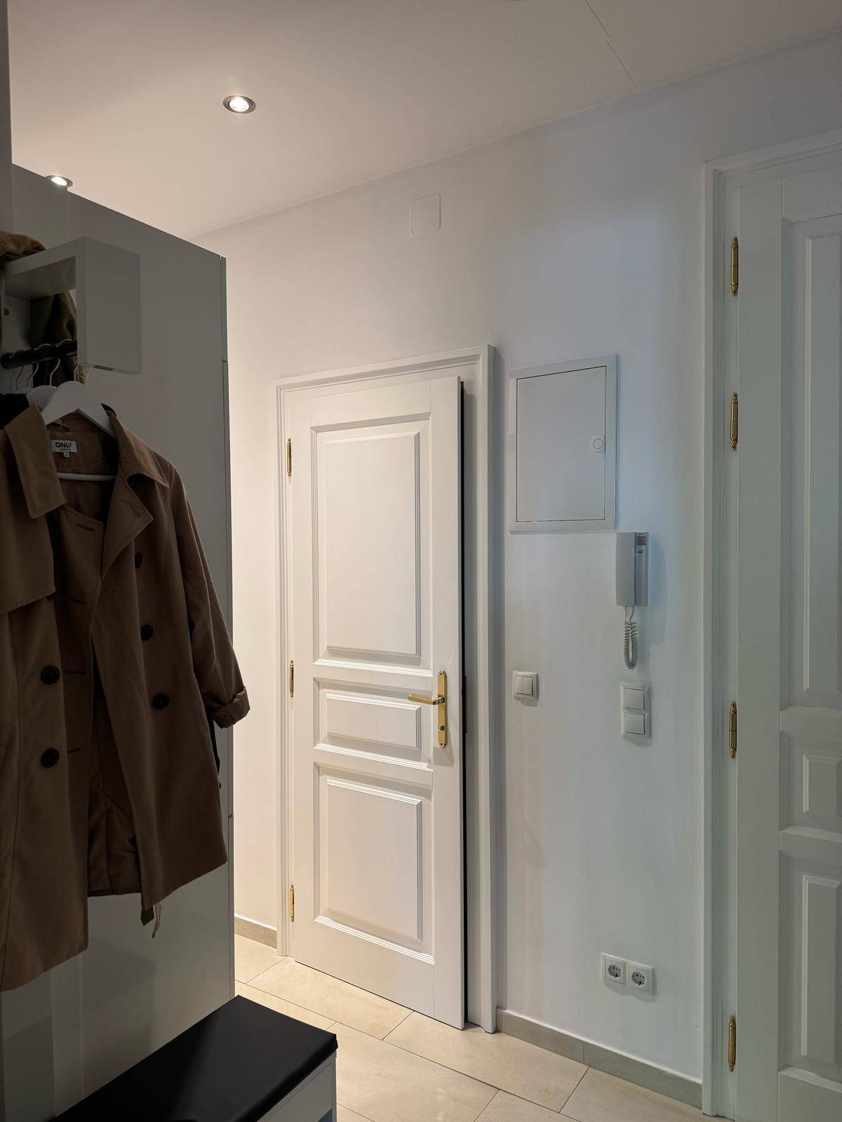 Heller Eingangsbereich mit Garderobe, weißen Türen und Fliesenboden.
