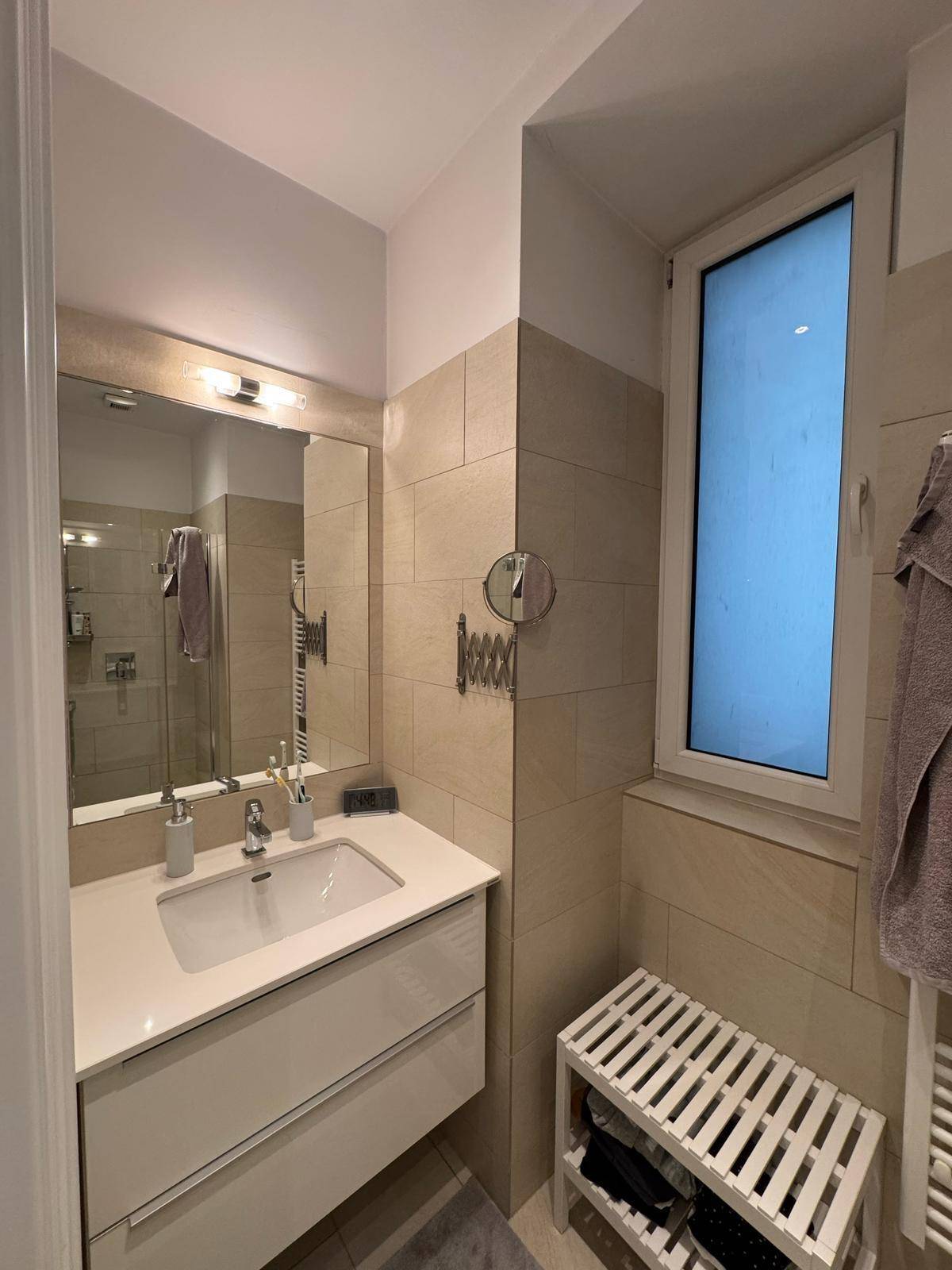 Modernes Badezimmer mit Einzelwaschbecken, Spiegel, beigefarbenen Fliesen und Fenster.