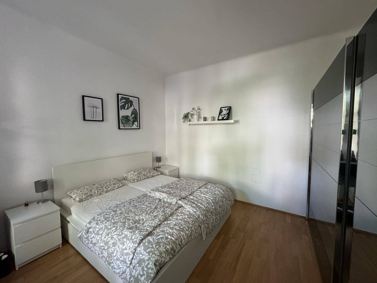 Helles Schlafzimmer mit Doppelbett, Nachttischen und großem Spiegelschrank.