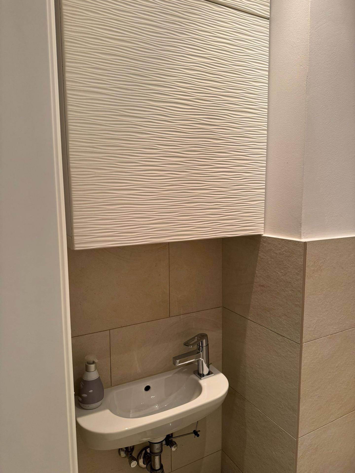Kleines Waschbecken in einem Gäste-WC mit beigefarbenen Fliesen und Unterschrank.
