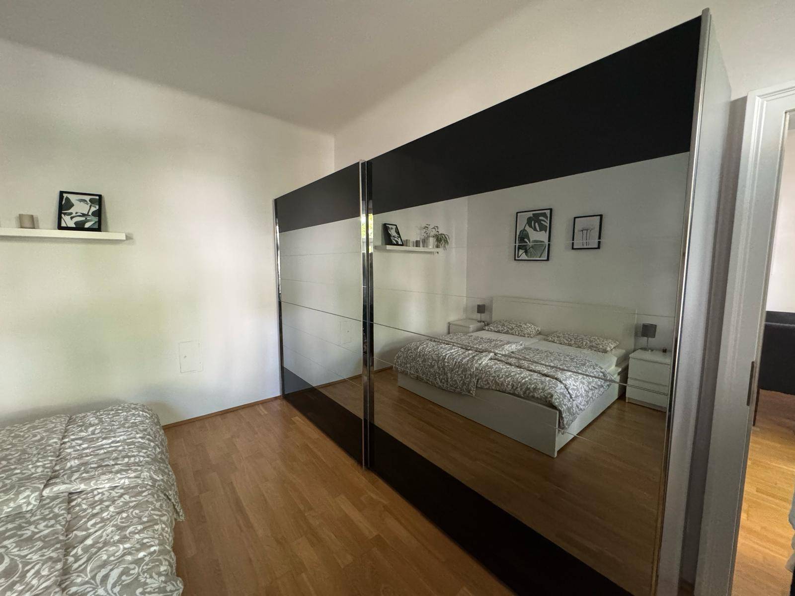 Schlafzimmer mit großem Spiegelschrank, der das Bett reflektiert, und Holzboden.