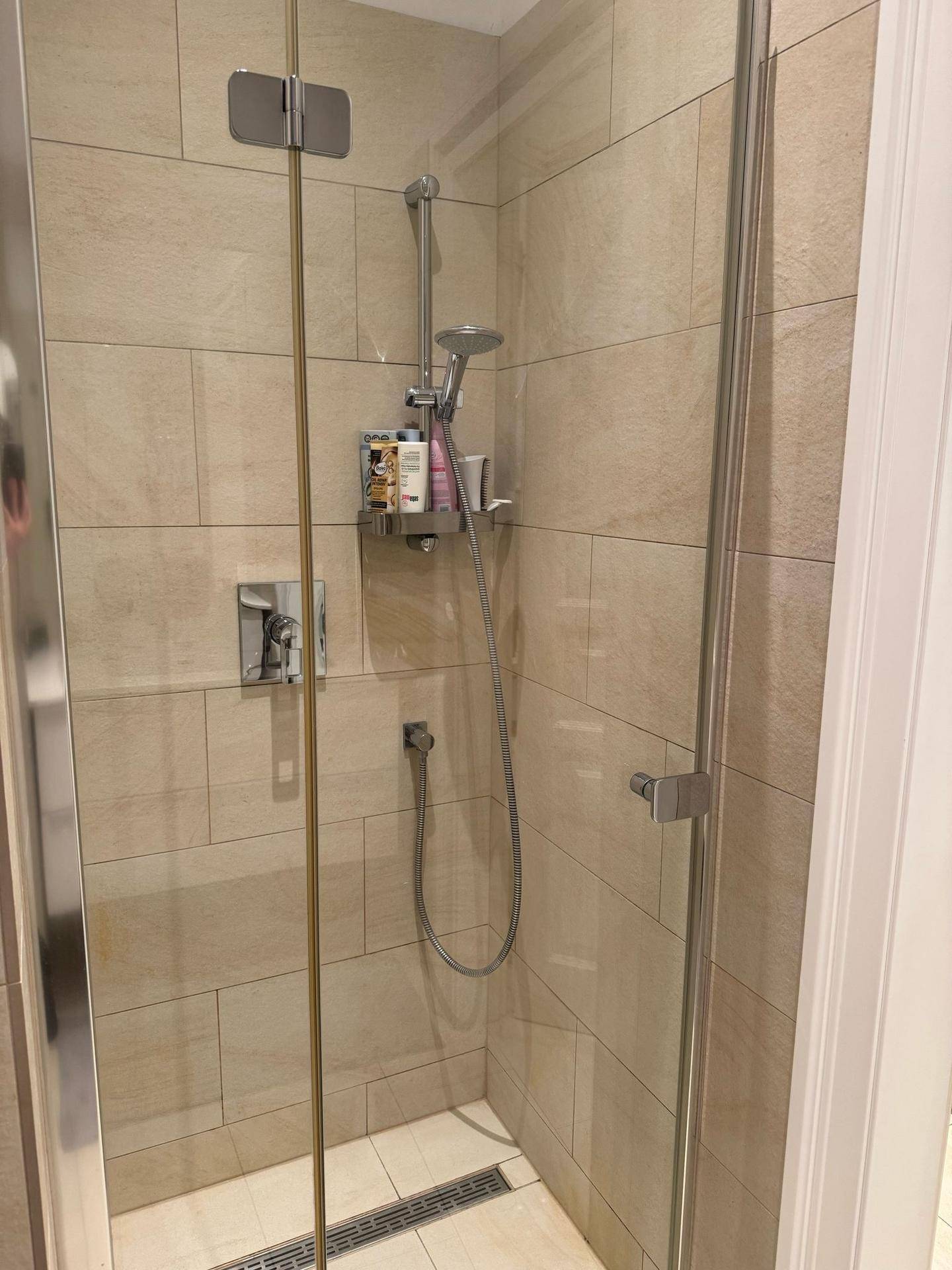 Moderne Duschkabine mit Glaswänden und beigefarbenen Fliesen im Badezimmer.