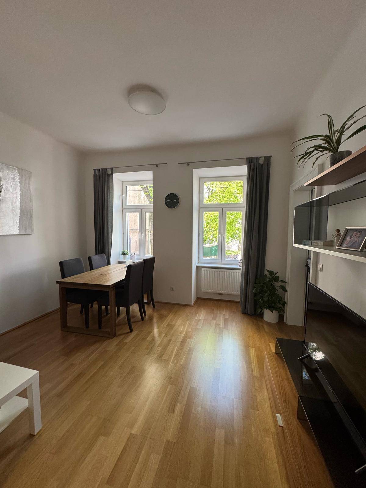 Heller Wohn-Essbereich mit Holztisch, Stühlen und großen Fenstern mit Blick ins Grüne.
