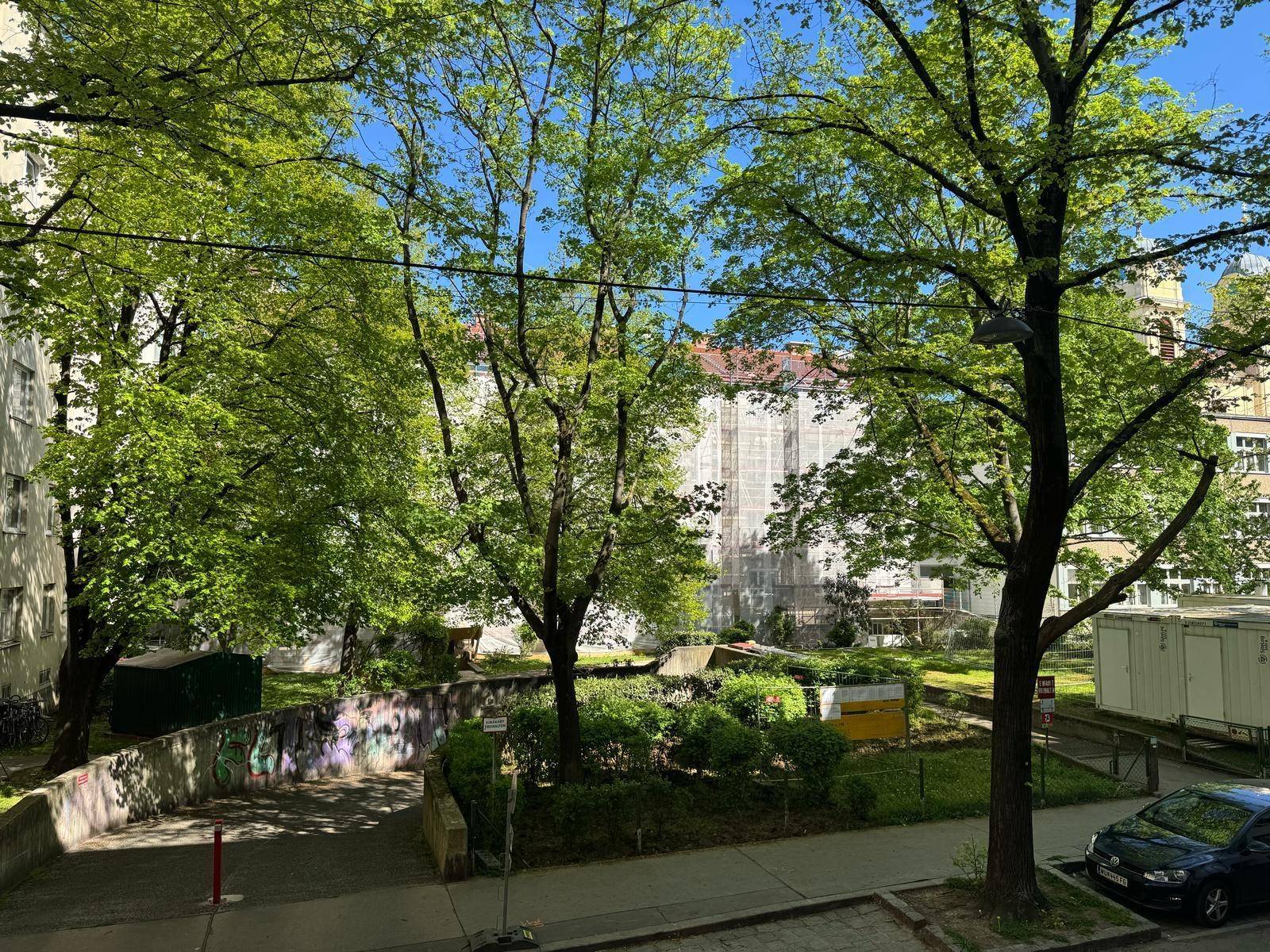 Grüner Innenhof mit Bäumen und einem Gebäude im Hintergrund, das renoviert wird.