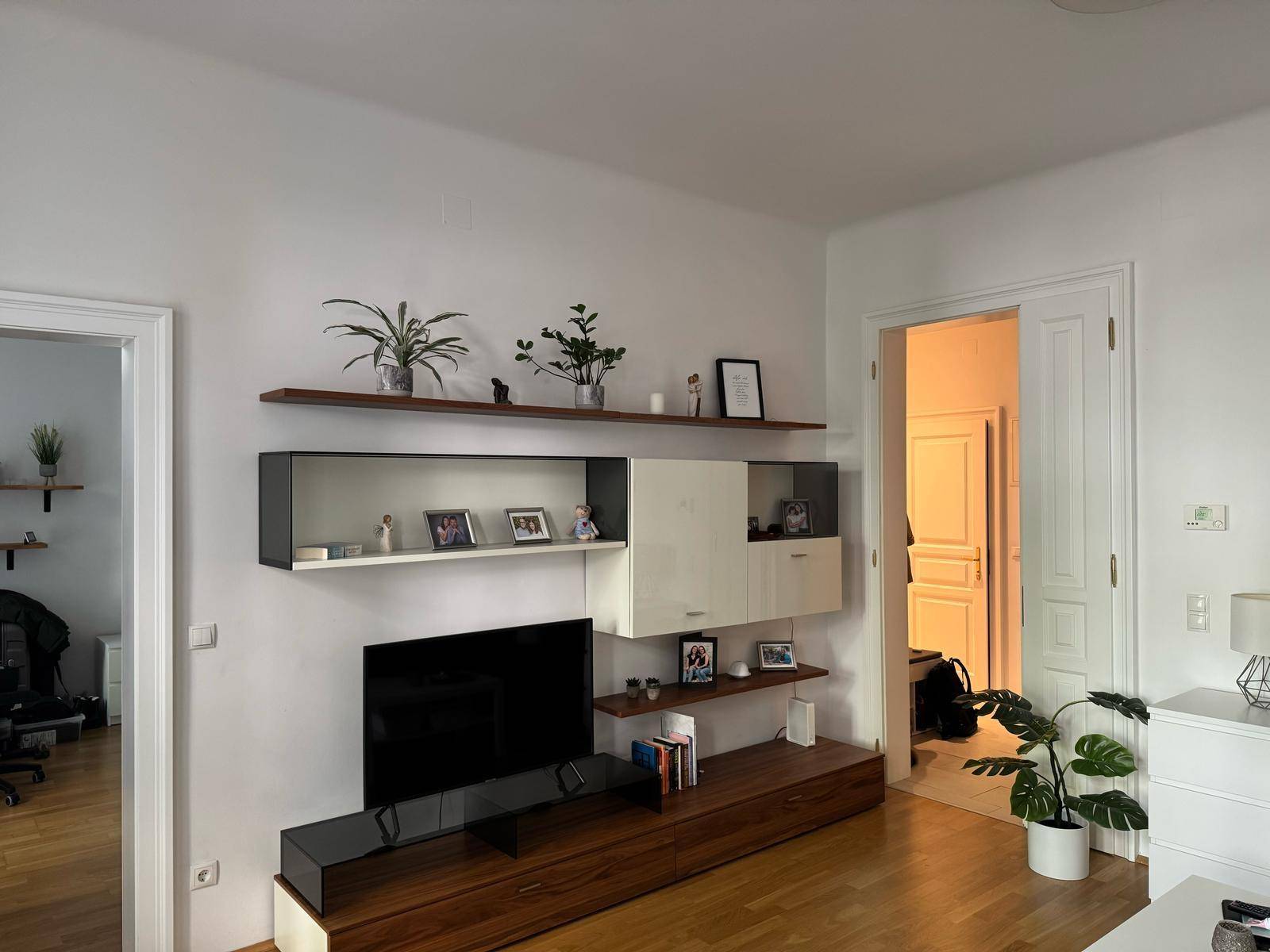 Helles Wohnzimmer mit modernem TV-Möbel, Regalen und Holzboden, das eine gemütliche Atmosphäre schafft.