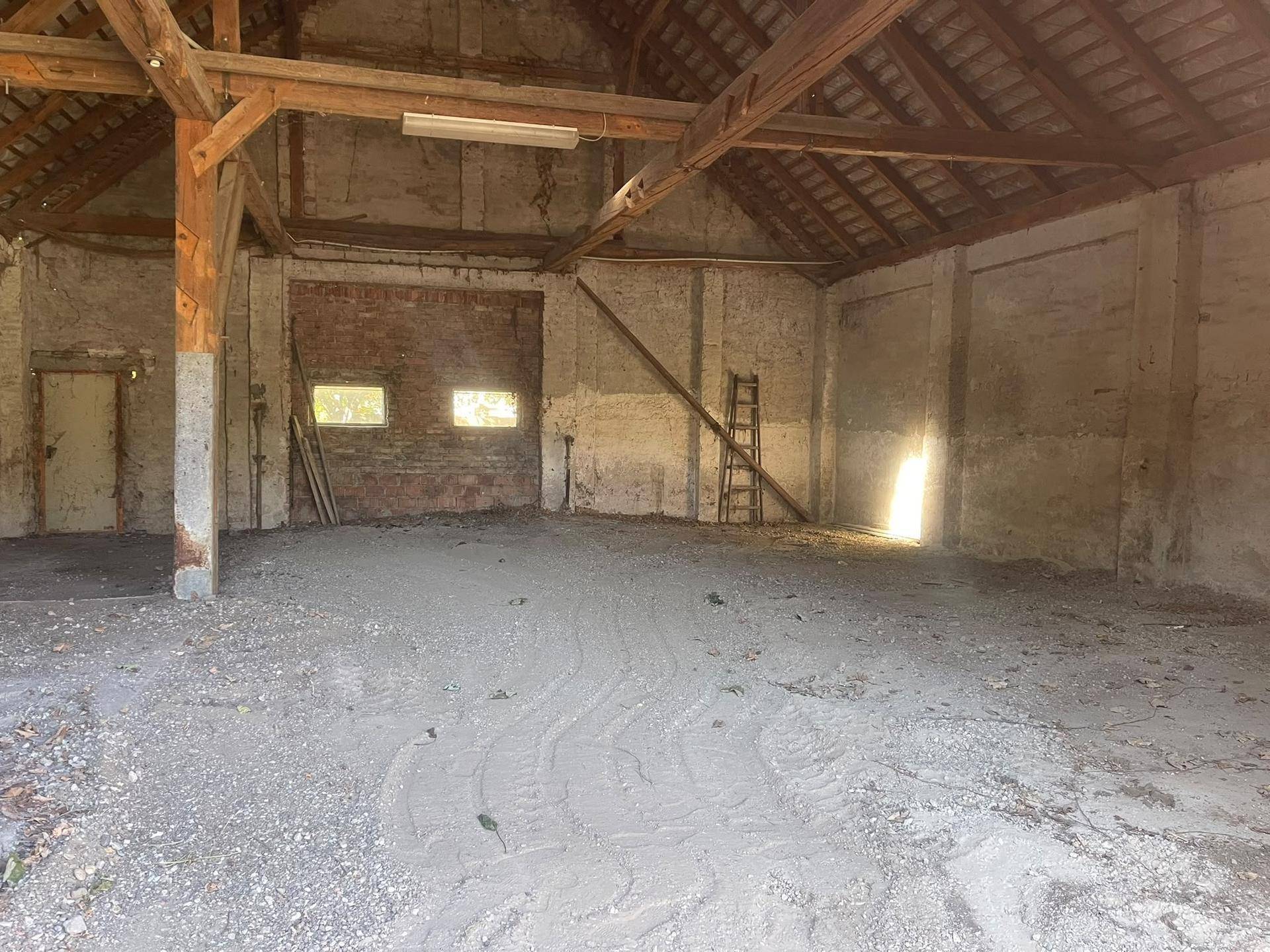Geräumiger, unfertiger Innenraum mit Holzdachstuhl und kleinen Fenstern, bereit für Renovierung.