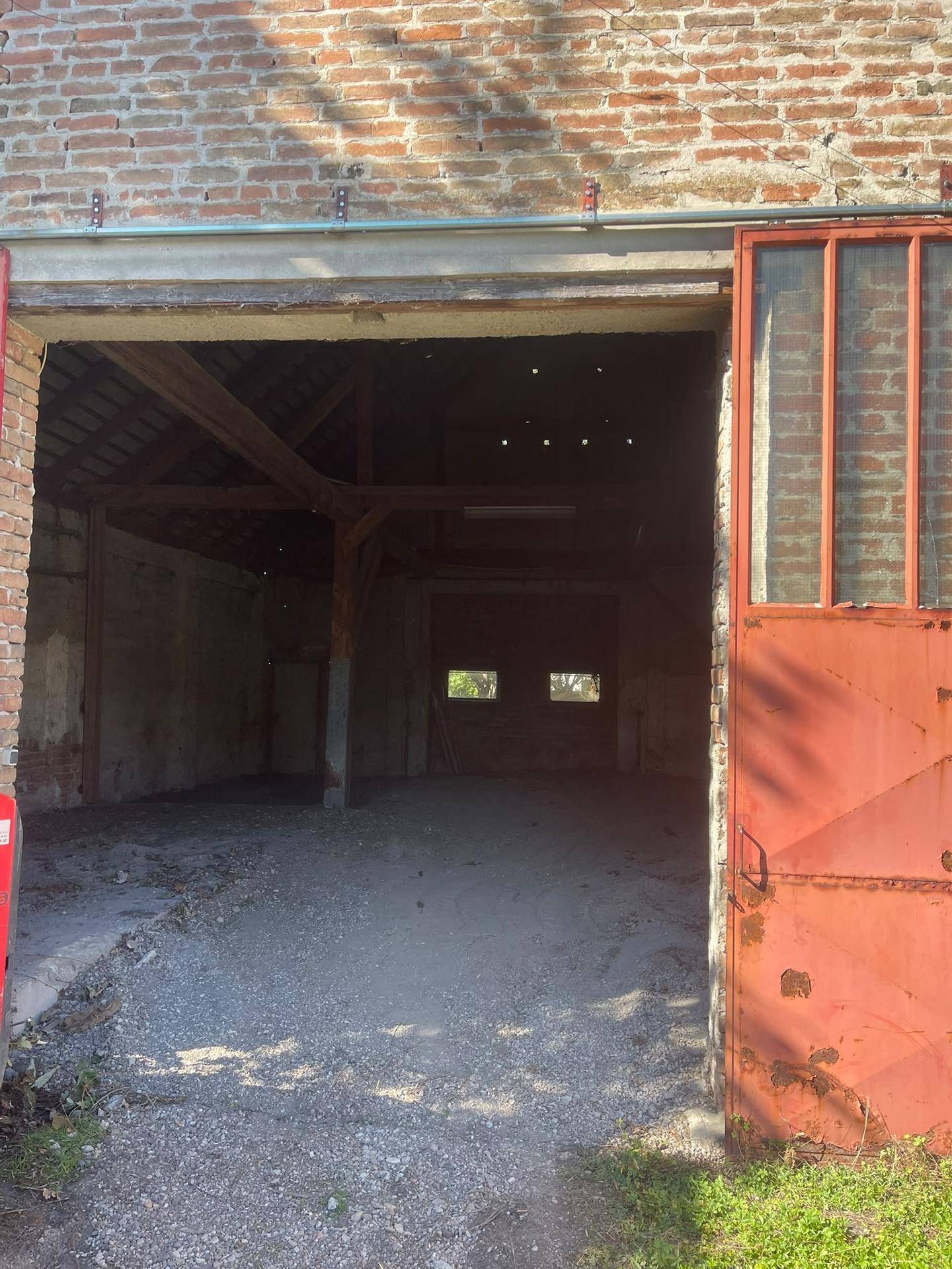 Blick durch die offenen roten Tore in das Innere des alten Backsteingebäudes mit Holzbalken.