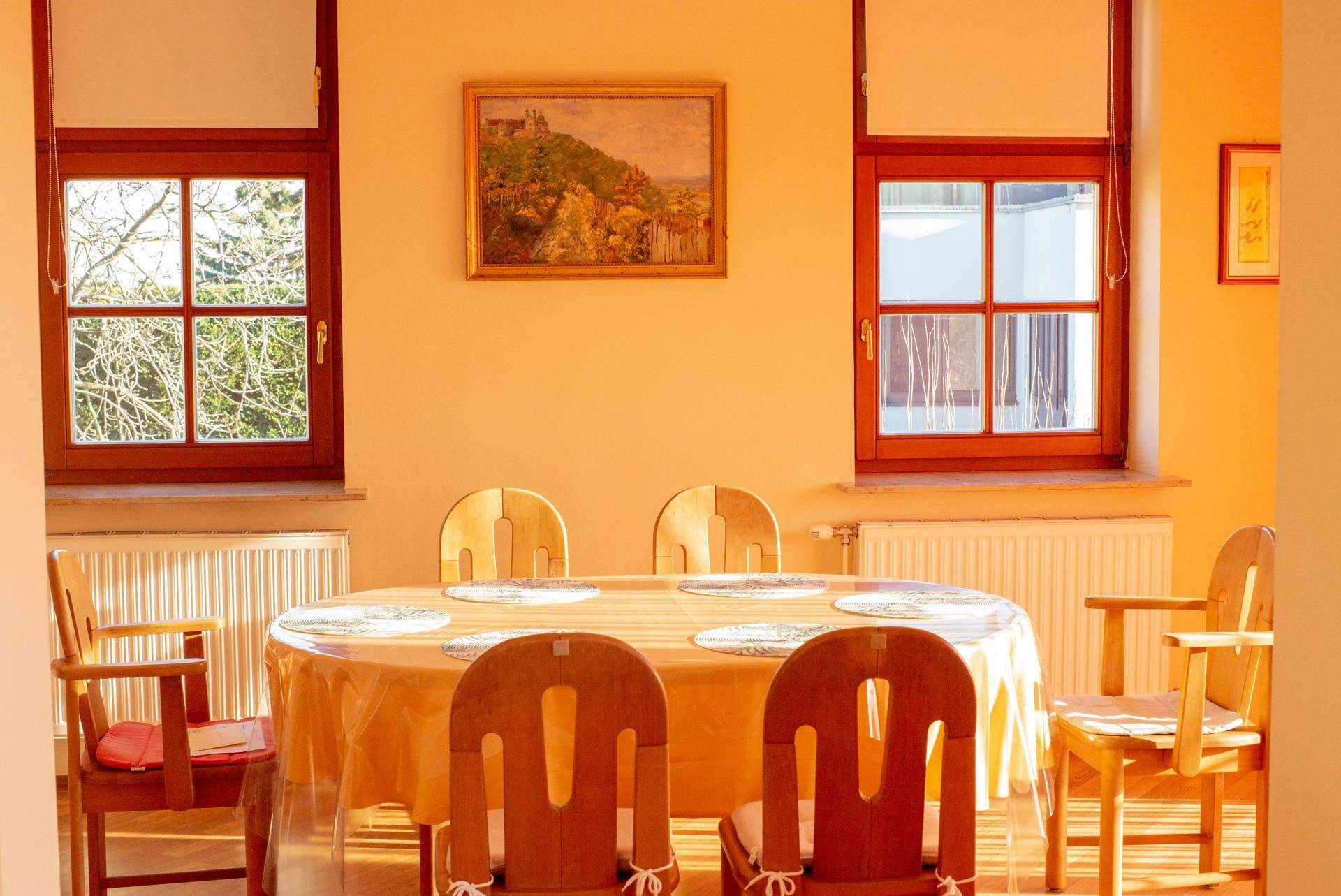 Esszimmer mit ovalem Holztisch, passenden Stühlen und zwei Fenstern für viel Licht.