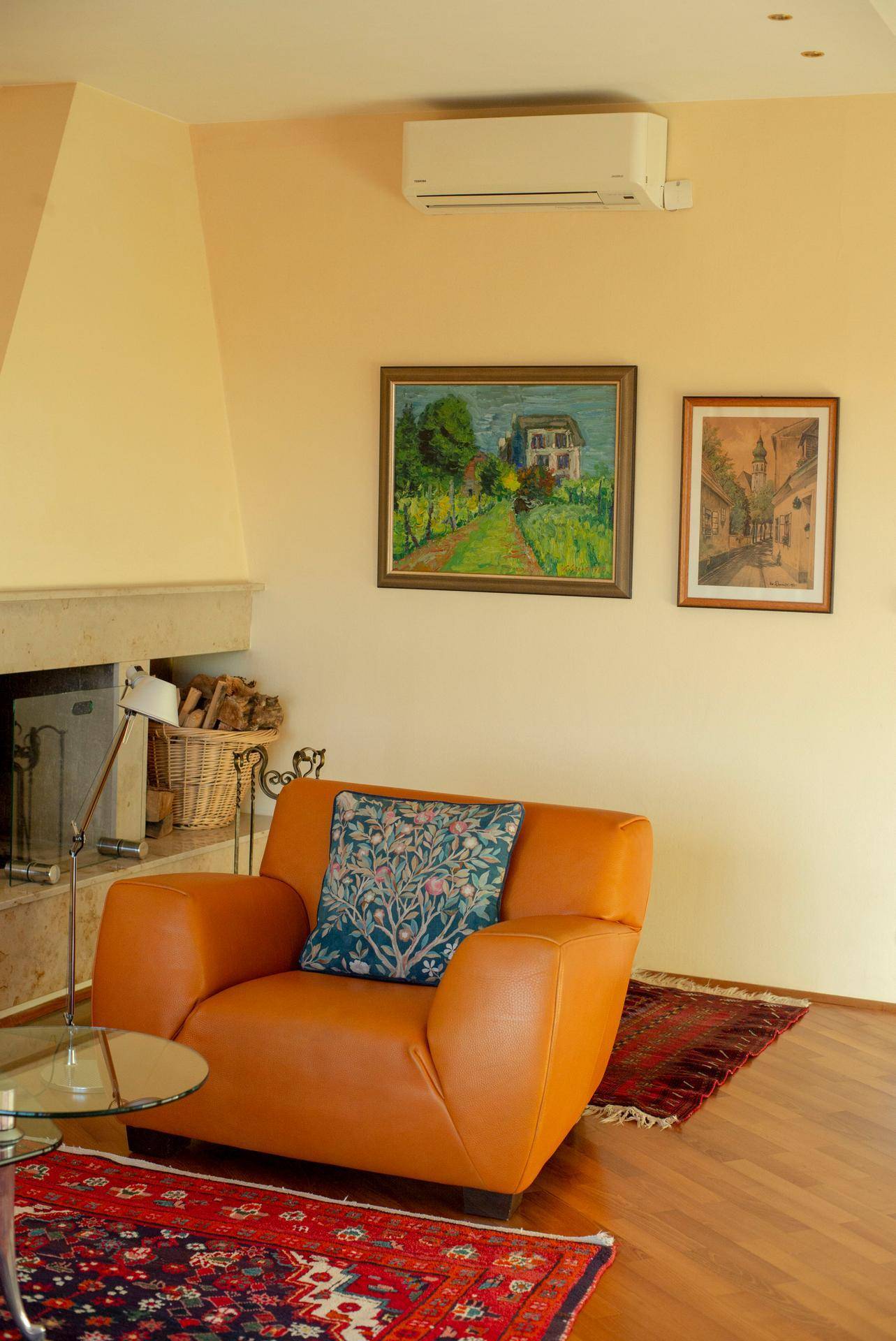 Wohnzimmer mit Kamin, Ledersessel, Kunstwerken an der Wand und Klimaanlage.