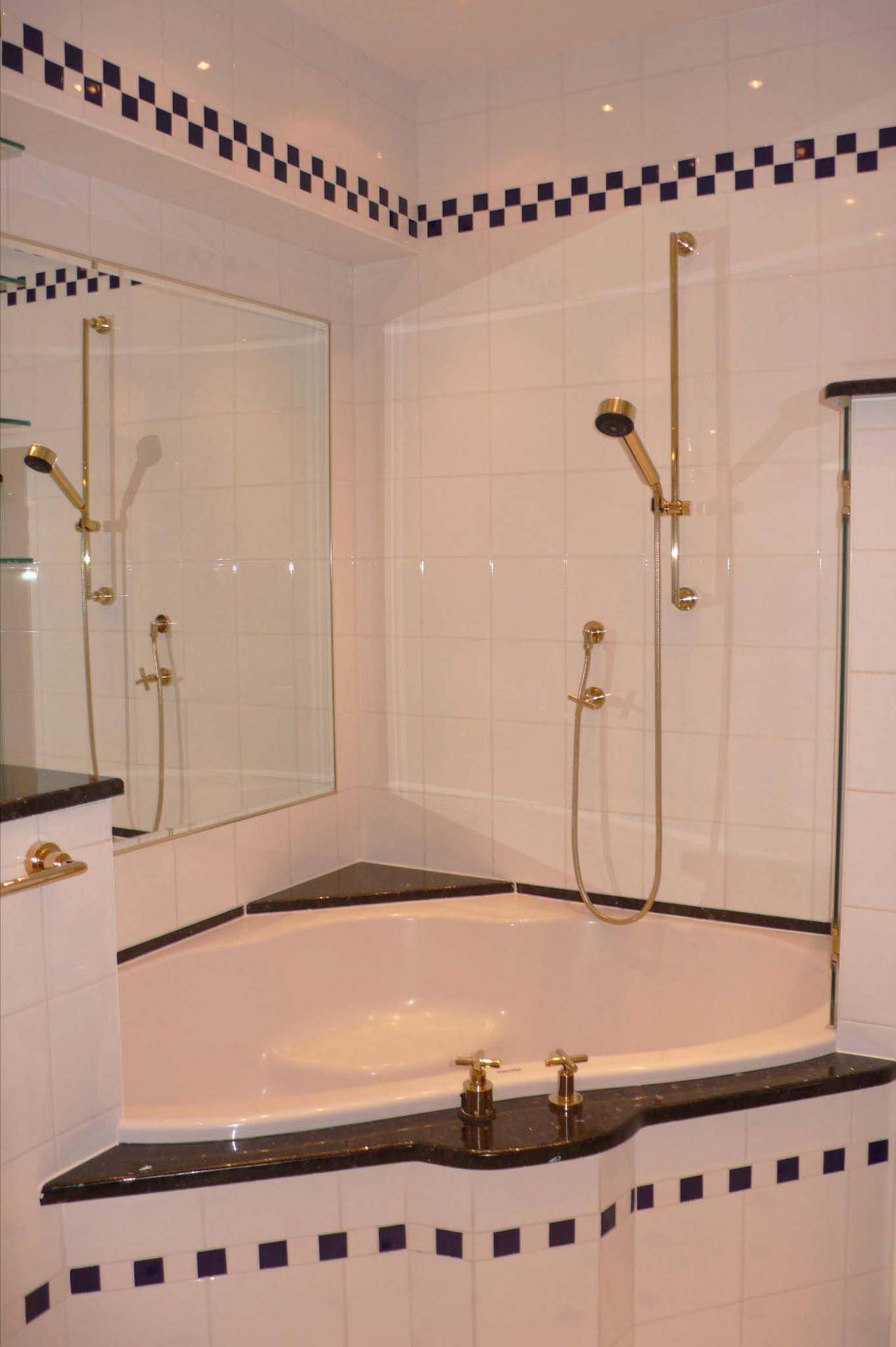 Badezimmer mit Eckbadewanne, Duschfunktion und goldfarbenen Armaturen.