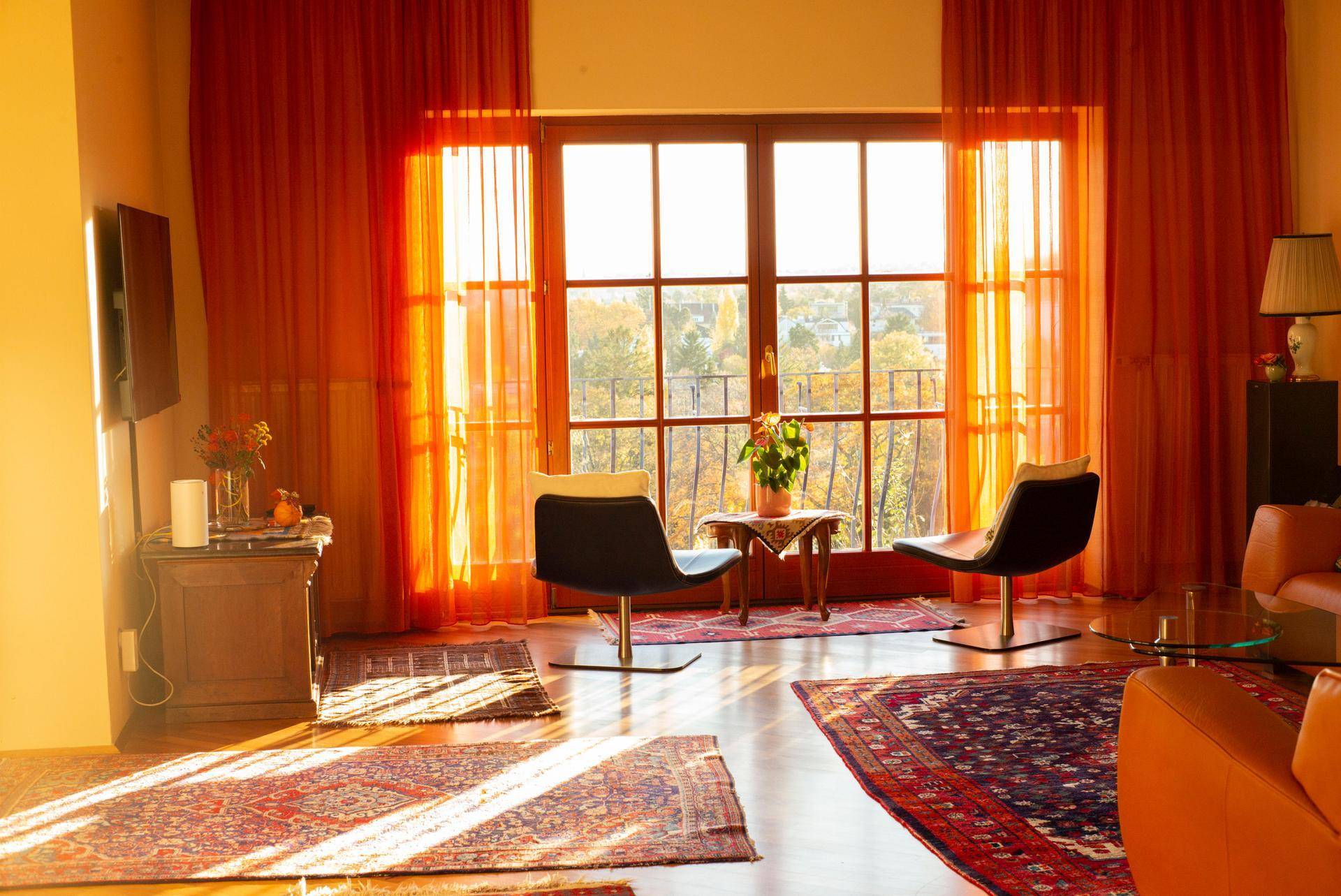 Helles Wohnzimmer mit orangefarbenen Vorhängen, Holzboden und Blick ins Grüne.
