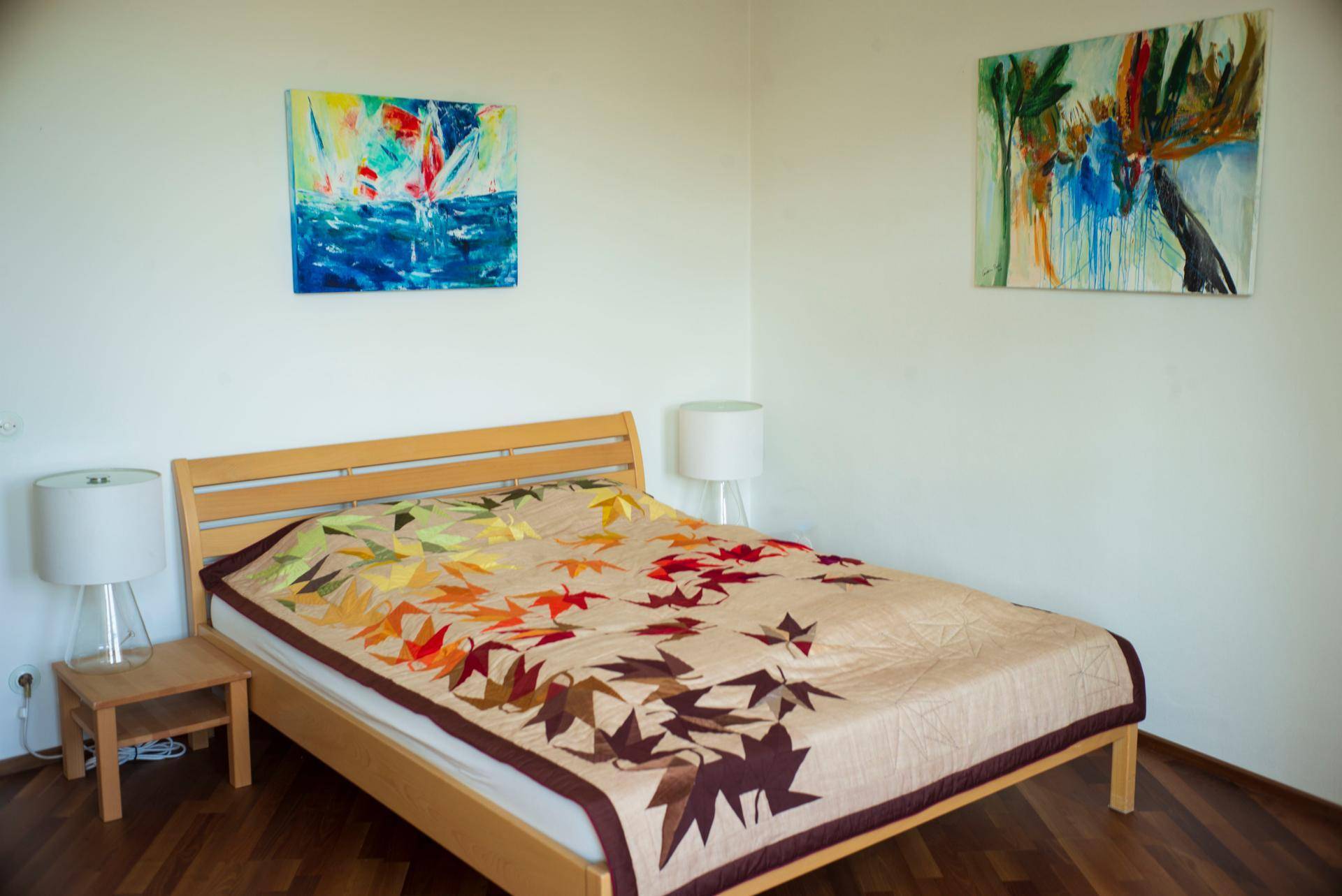 Helles Schlafzimmer mit modernem Holzbett, Nachttischen und farbenfrohen Bildern.