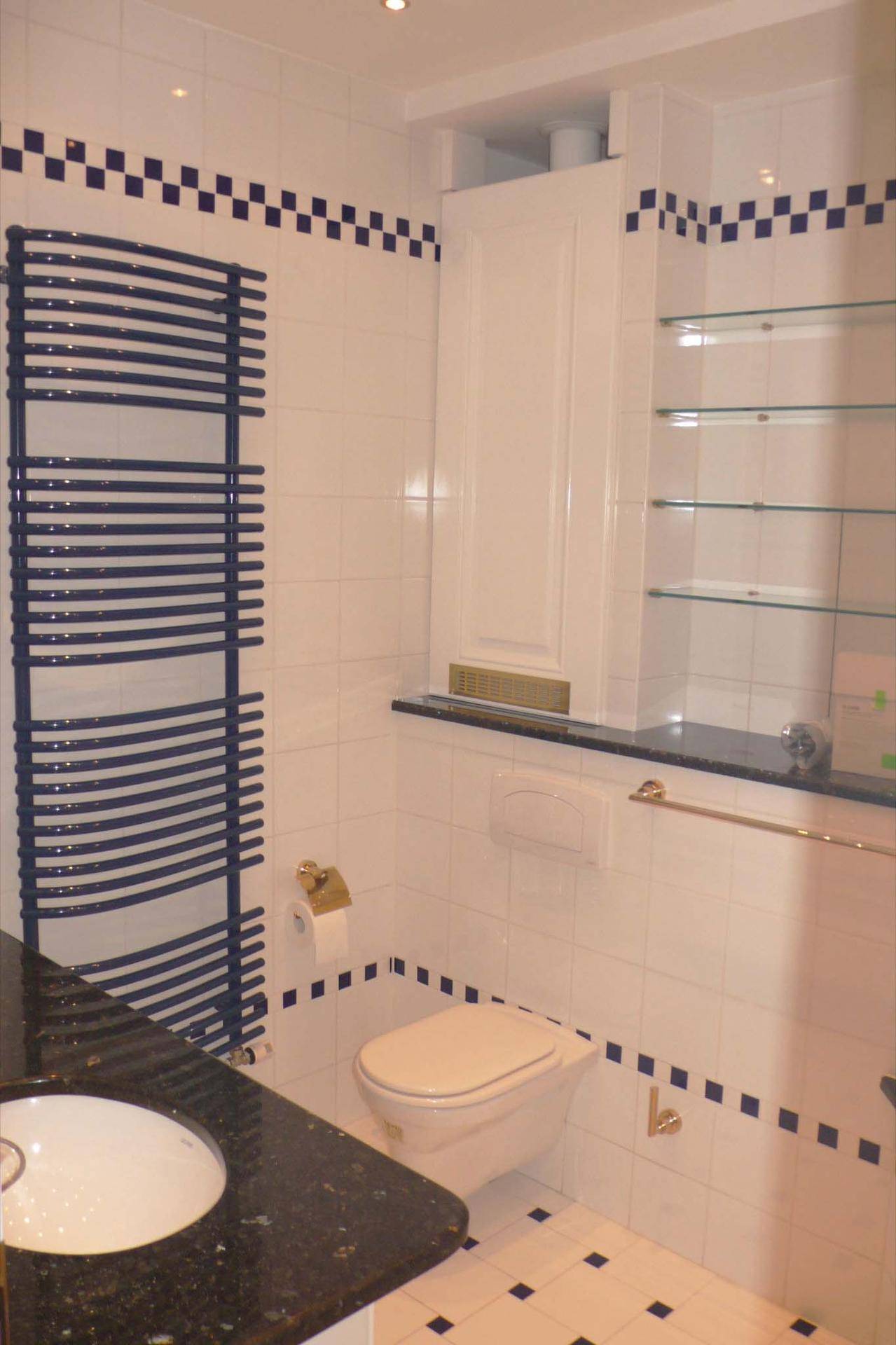 Badezimmer mit Wand-WC, Einbauschrank und blauen Akzentfliesen.