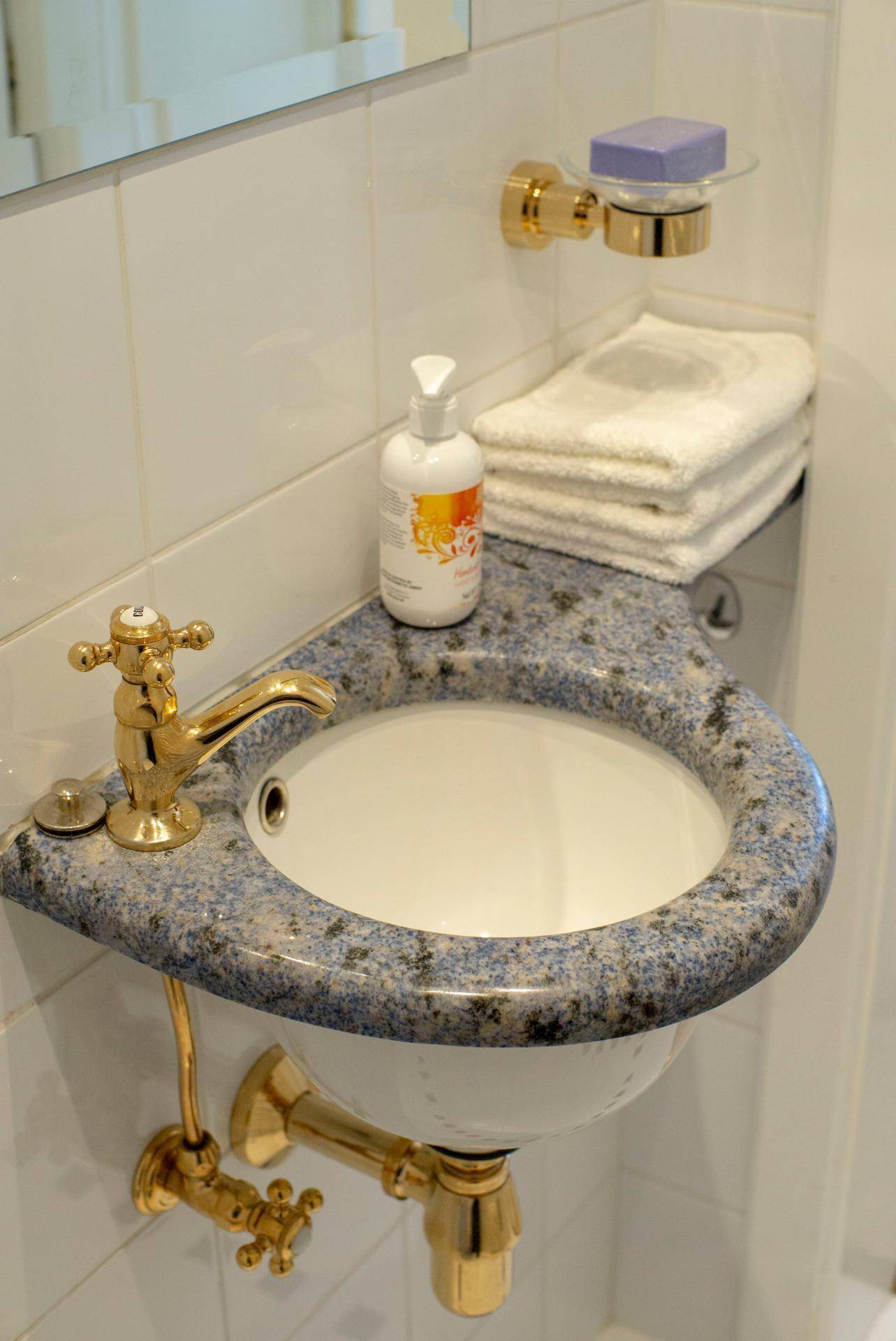 Detailansicht des Waschbeckens im Gäste-WC mit goldfarbenen Armaturen und gemusterter Ablage.