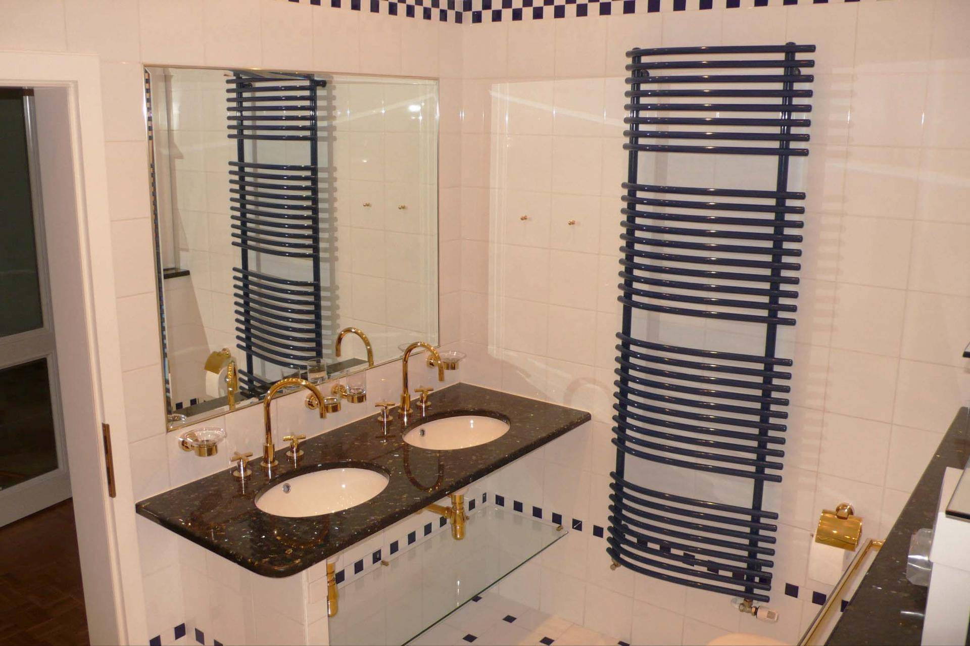 Modernes Badezimmer mit Doppelwaschbecken, dunkler Granitplatte und blauem Handtuchheizkörper.