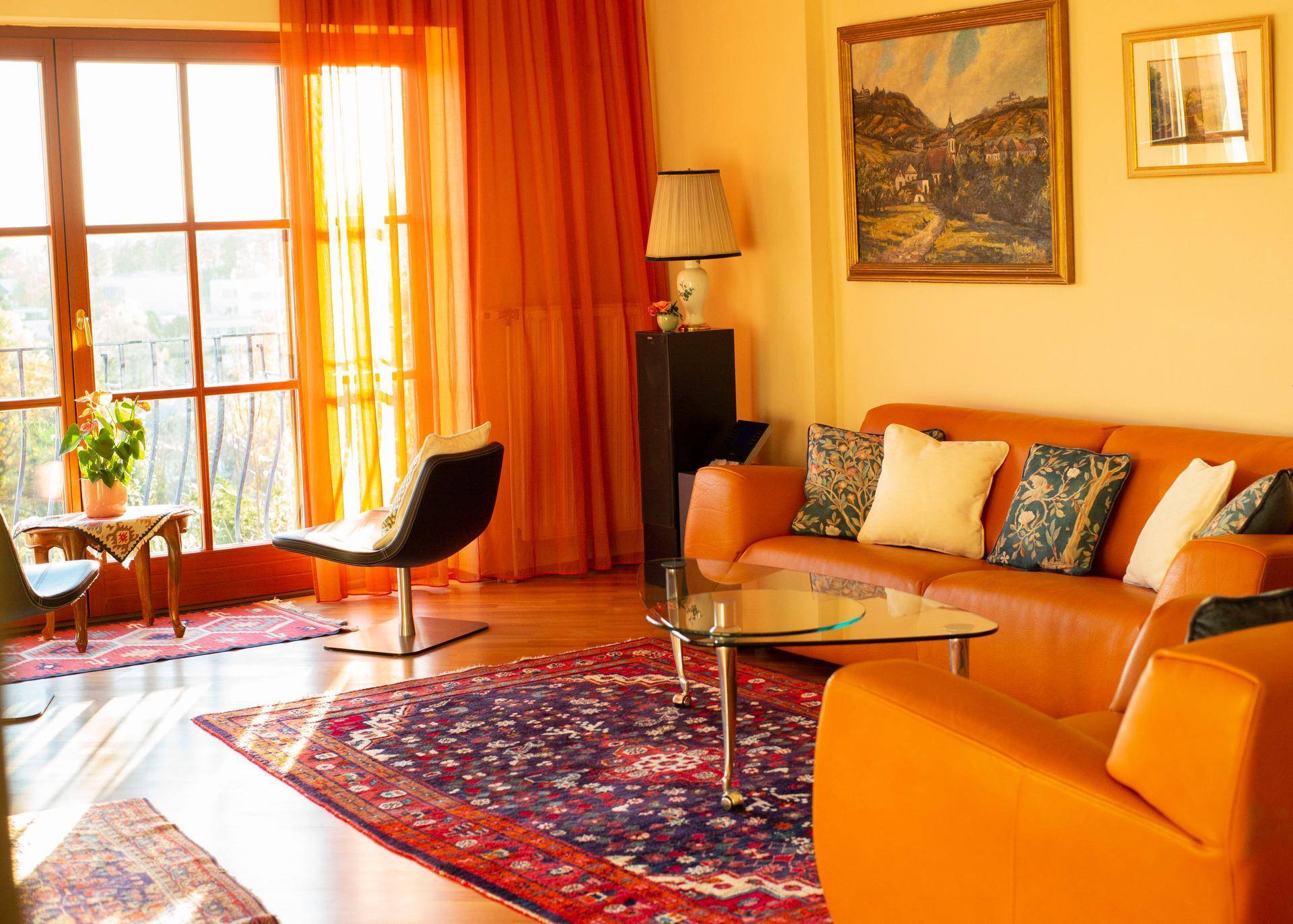 Lichtdurchflutetes Wohnzimmer mit orangefarbenen Ledersofas, Holzboden und großem Fenster.