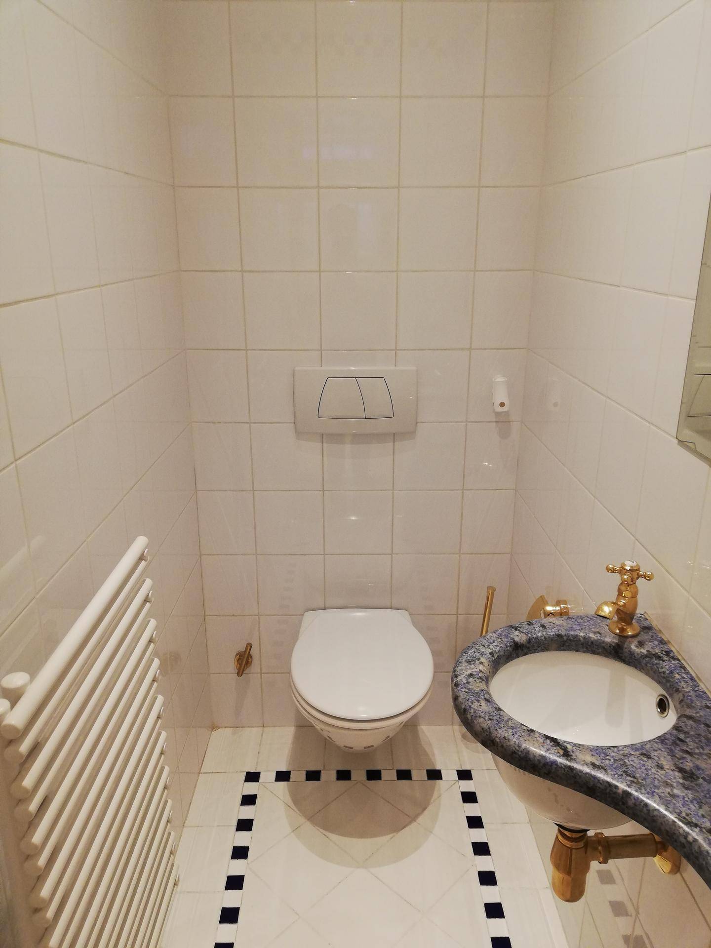 Kleines Gäste-WC mit weißen Fliesen, Wand-WC und farbigem Waschbecken.
