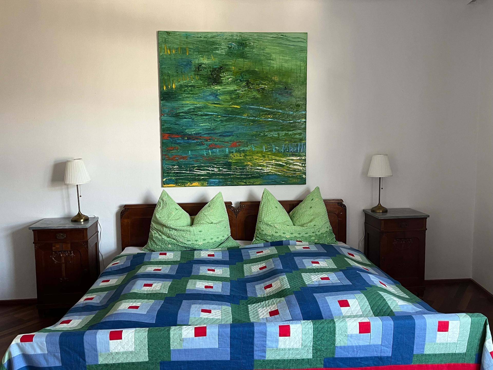Gemütliches Schlafzimmer mit Doppelbett, Nachttischen und farbenfrohem Kunstwerk.