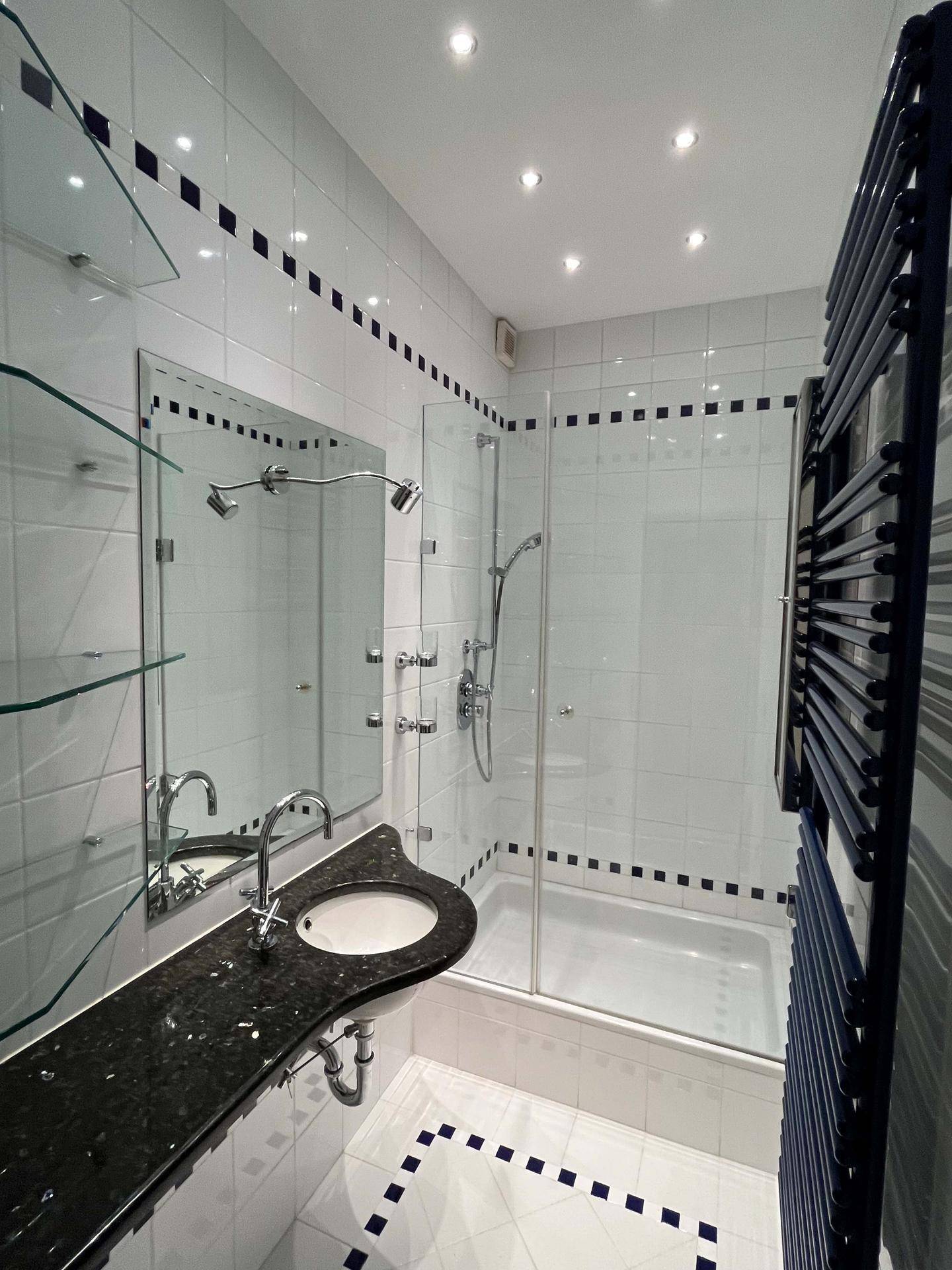 Modernes Badezimmer mit Einzelwaschbecken, Duschkabine und blauem Handtuchheizkörper.