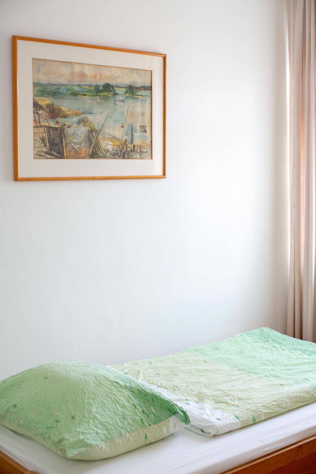 Nahaufnahme eines Bettes mit grüner Bettwäsche und einem gerahmten Bild an der weißen Wand.