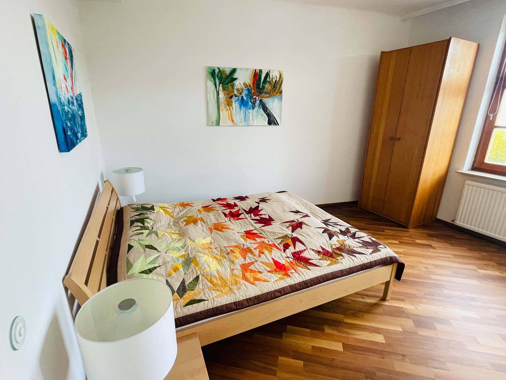 Schlafzimmer mit Holzbett, Kleiderschrank und farbenfroher Bettdecke.