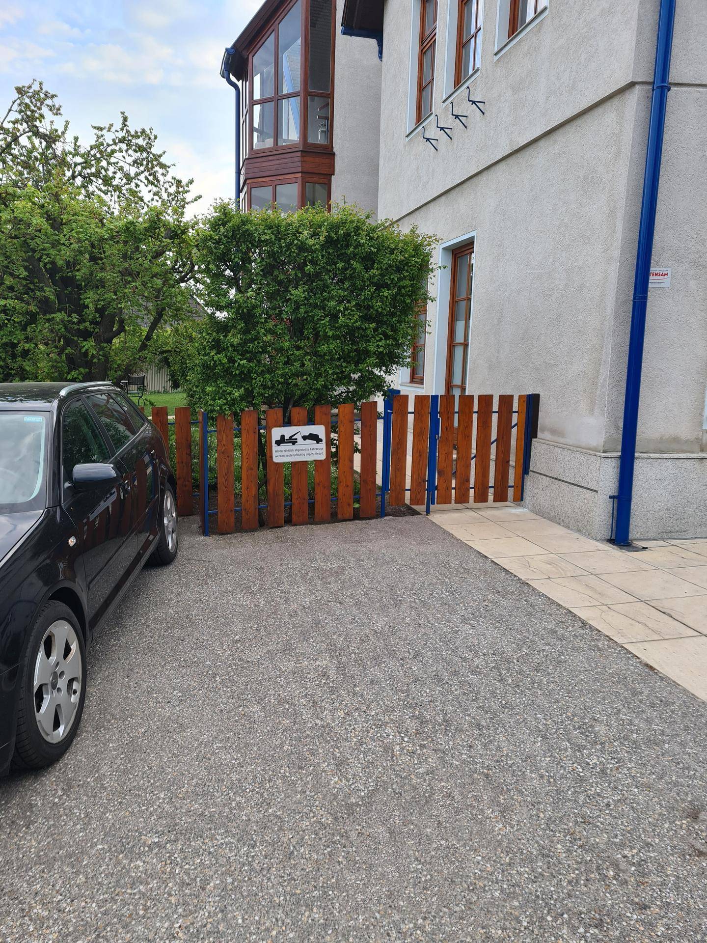 Außenansicht eines Hauses mit Schotterauffahrt, schwarzem Auto und einem Holzzaun.