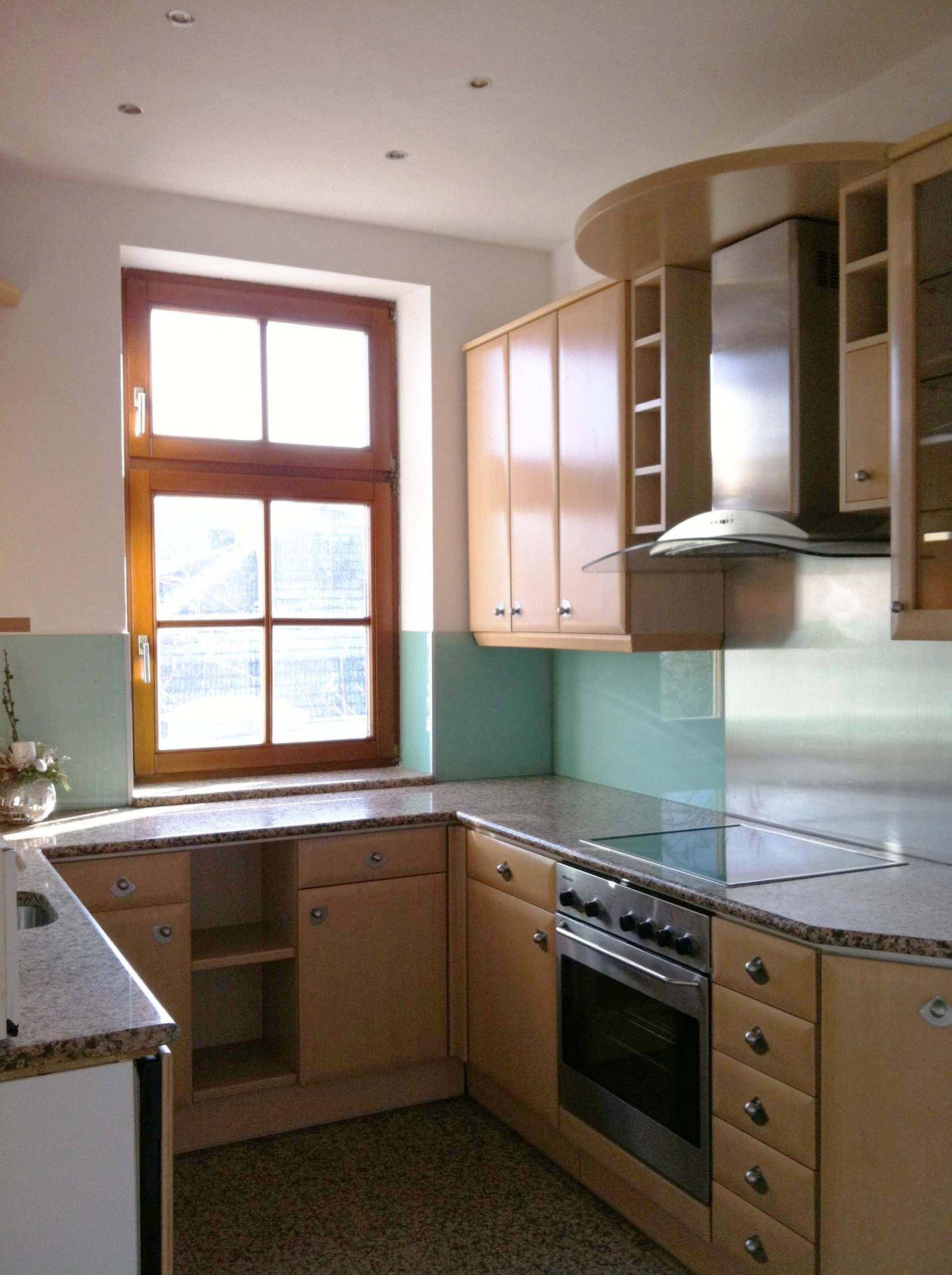 Helle Küche mit Holzschränken, Granitarbeitsplatten und einem Fenster mit Tageslicht.