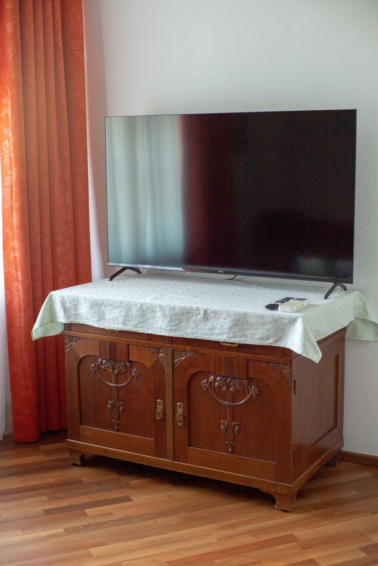 Antiker Holzschrank mit Fernseher und roten Vorhängen im Schlafzimmer.