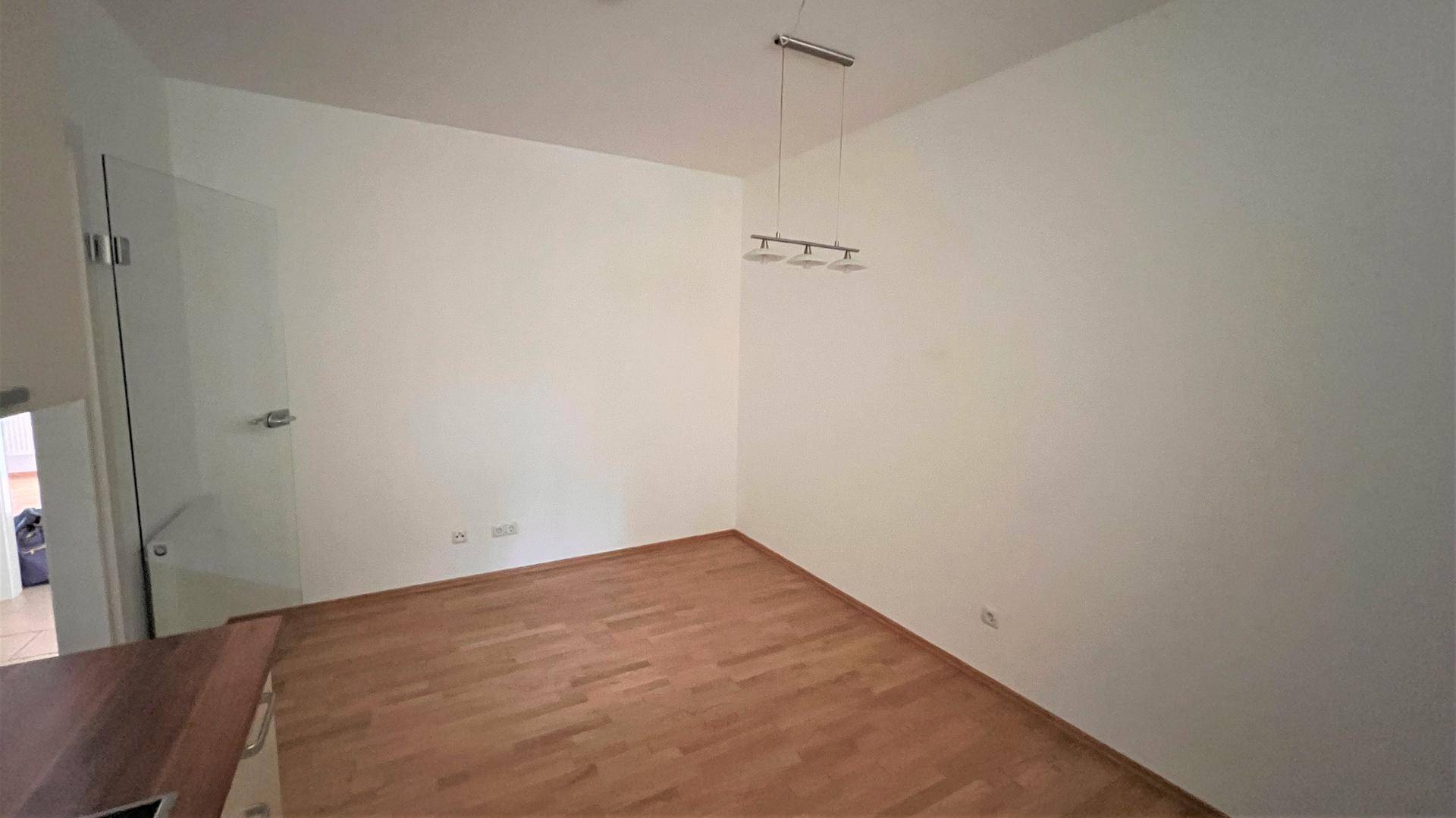Heller, leerer Wohnbereich mit Parkettboden und einer modernen Glasabtrennung.