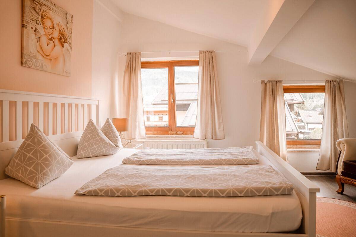 Helles Schlafzimmer im Dachgeschoss mit Doppelbett, schrägen Decken und Blick auf die umliegende Landschaft.