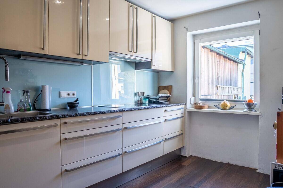 Funktionale Küche mit beigen Hochglanzschränken, dunkler Arbeitsplatte und Fenster.
