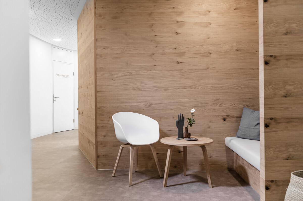 Gemütlicher Wartebereich mit Holzwandverkleidung, bequemer Sitzbank und modernem Stuhl, einladend und hell.