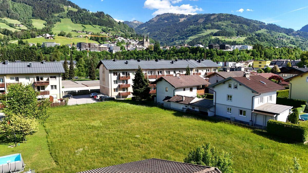 Weitläufige Grünfläche mit Blick auf umliegende Wohnhäuser und die beeindruckende Berglandschaft.