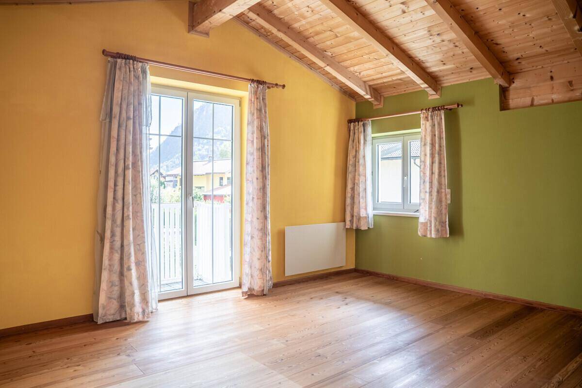 Geräumiges Schlafzimmer mit Holzbalkendecke, gelben Wänden und Zugang zum Balkon.