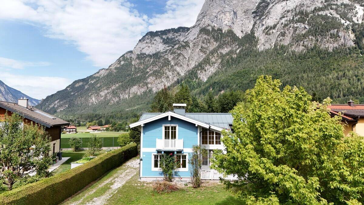 Blaues Haus in alpiner Landschaft mit Bergen und grünen Bäumen unter blauem Himmel.