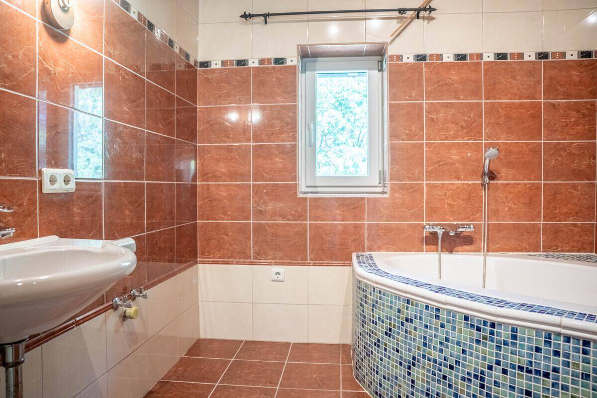Badezimmer mit braunen Fliesen, Badewanne und Fenster, in traditionellem Stil.