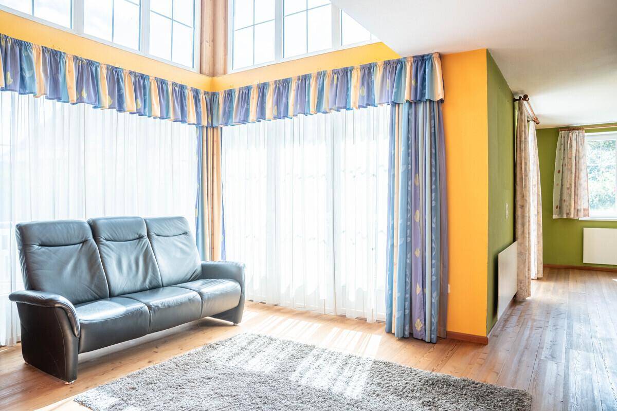 Helles Wohnzimmer mit großen Fenstern, Ledersofa und farbenfrohen Vorhängen.