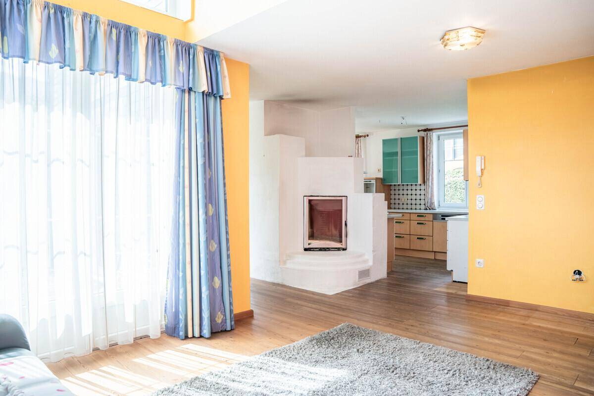 Offener Wohnbereich mit Kamin und Blick auf die Küche, mit Holzboden und gelben Wänden.