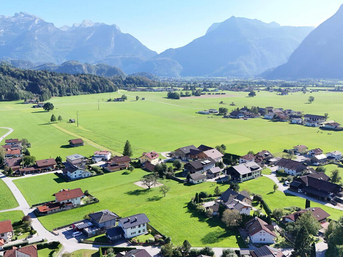 Luftaufnahme eines malerischen Dorfes, eingebettet in grüne Felder mit majestätischen Bergen im Hintergrund.