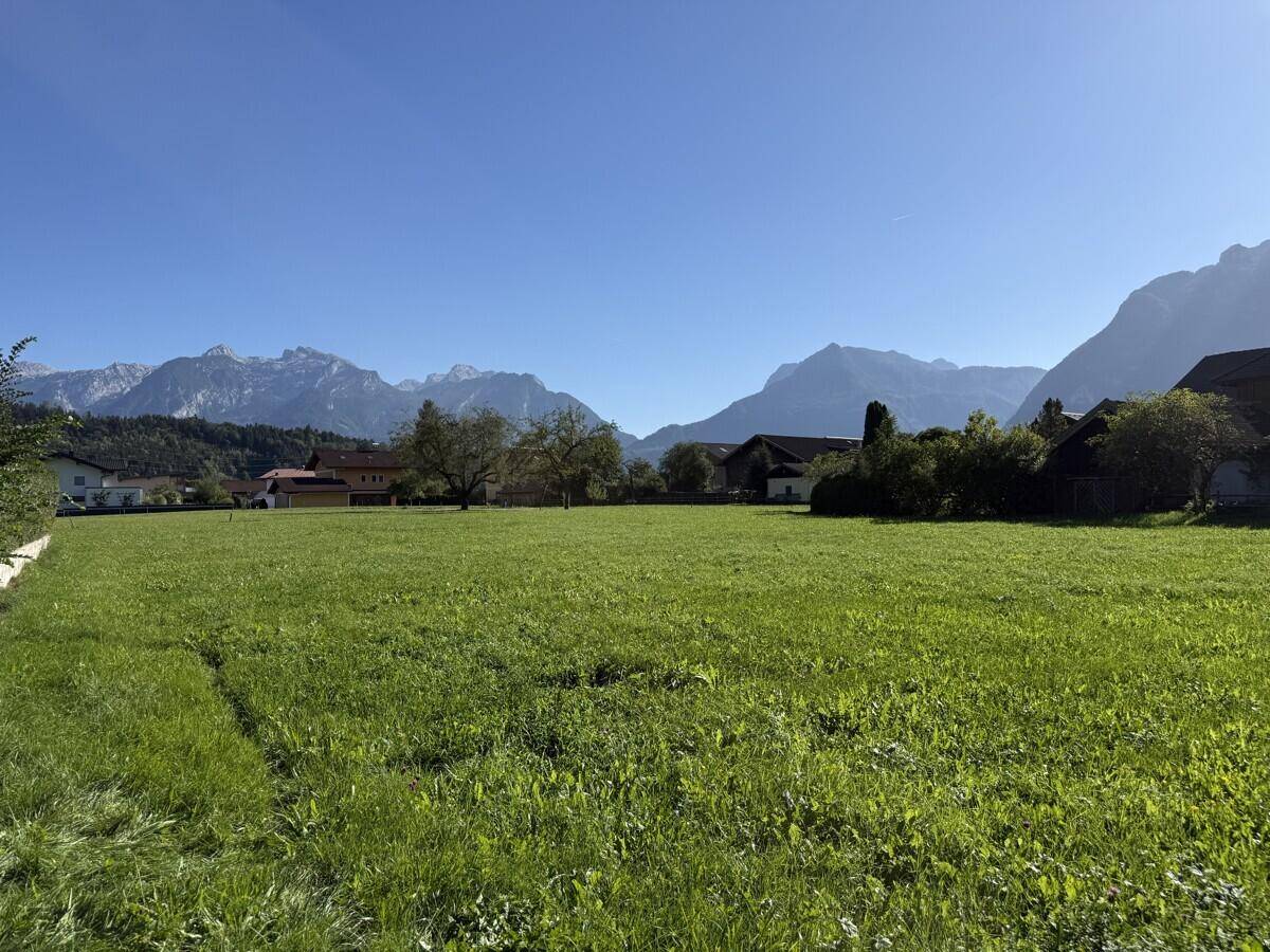 Sonniges grünes Feld mit Blick auf die umliegenden Häuser und die imposante Bergkette am Horizont.