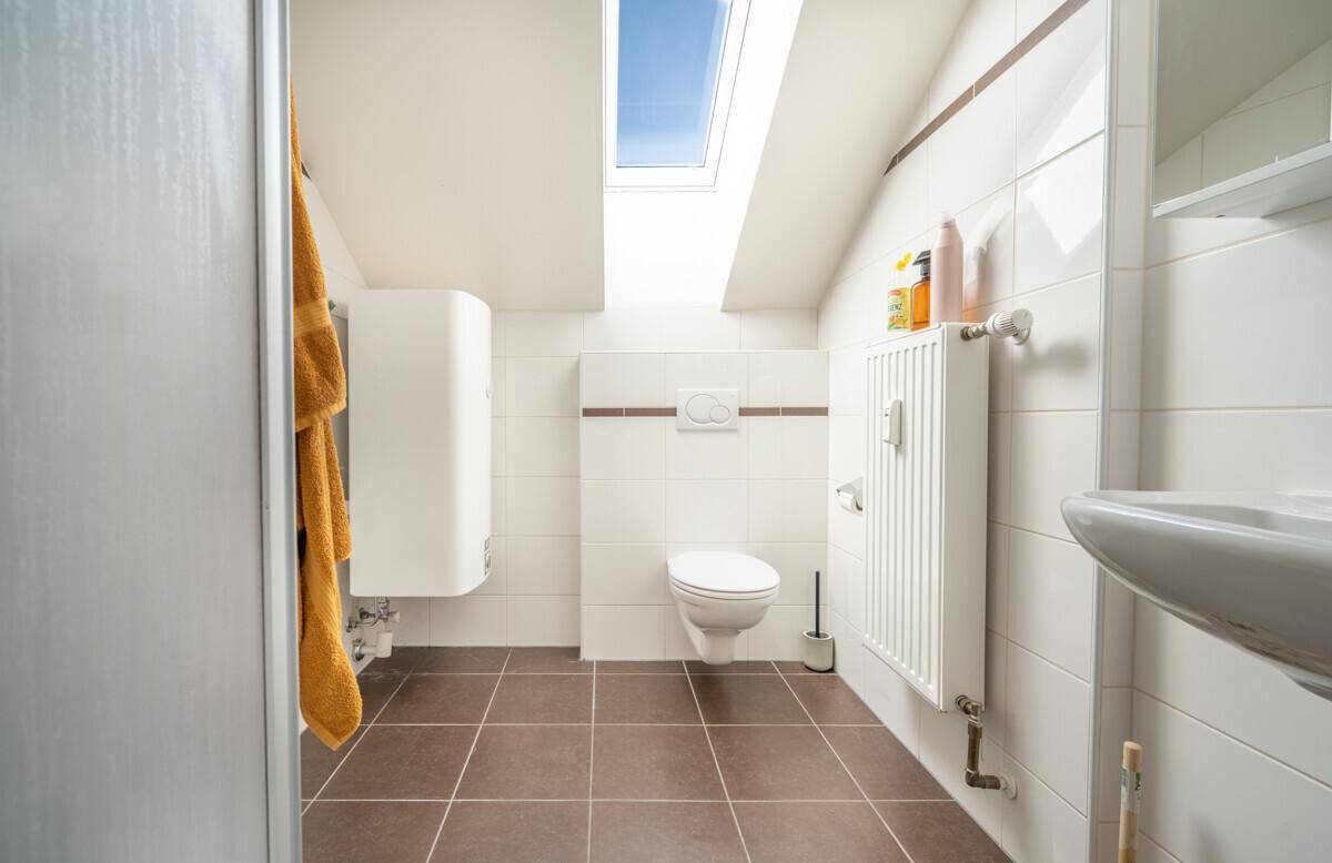 Modernes Badezimmer im Dachgeschoss mit Dusche, WC, Waschbecken und Dachfenster.