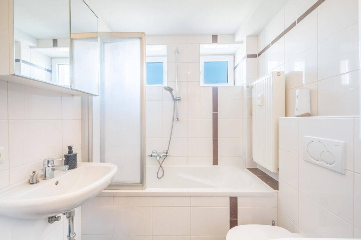 Helles Badezimmer mit Badewanne, integrierter Dusche, WC und Waschbecken.
