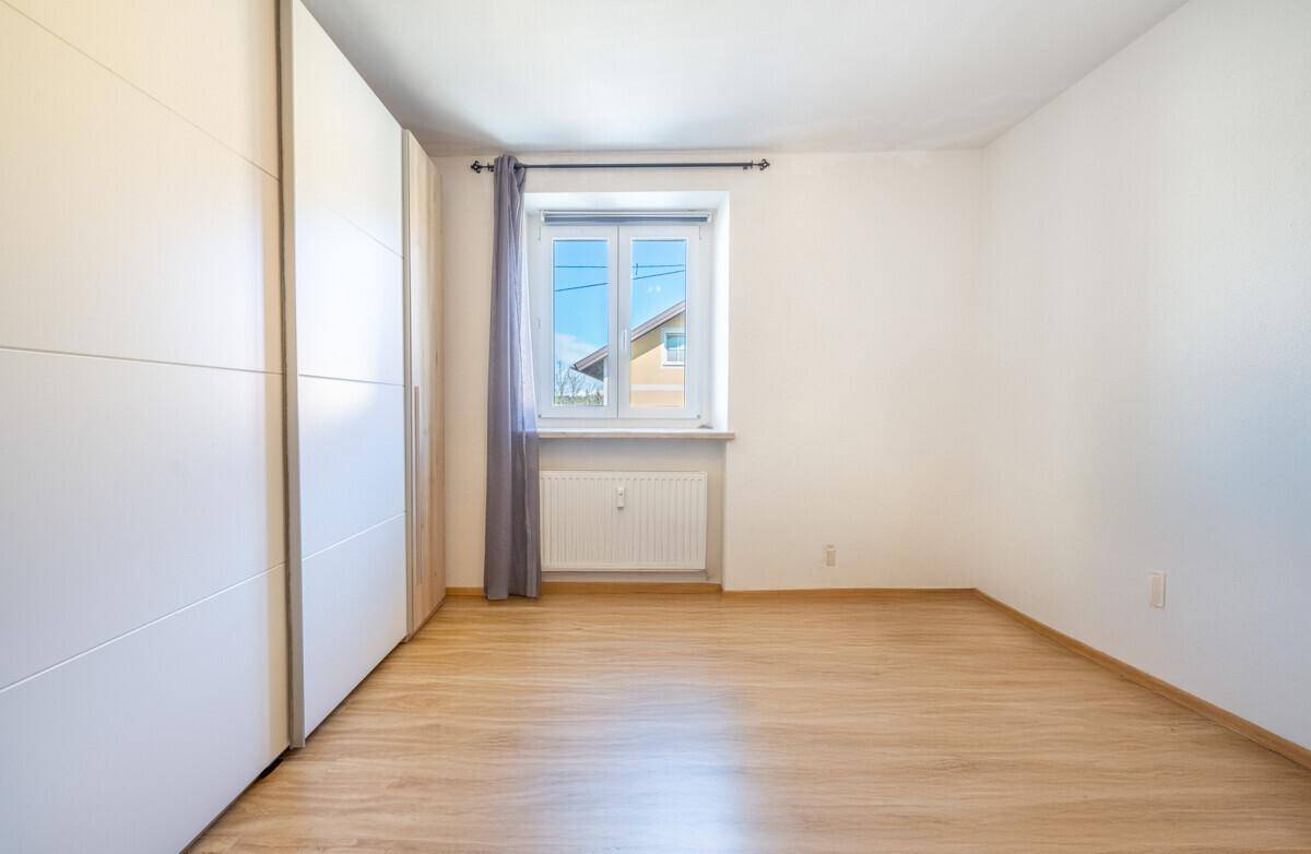 Geräumiges Schlafzimmer mit hellem Laminatboden, großem Fenster und Einbauschrank.