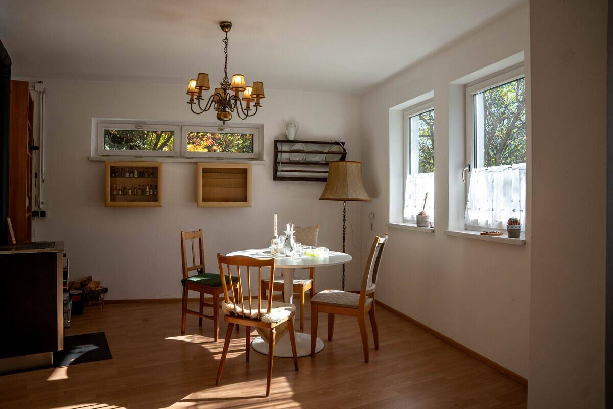 Gemütlicher Essbereich mit Holzboden, Kronleuchter und Fenstern mit Blick ins Grüne.