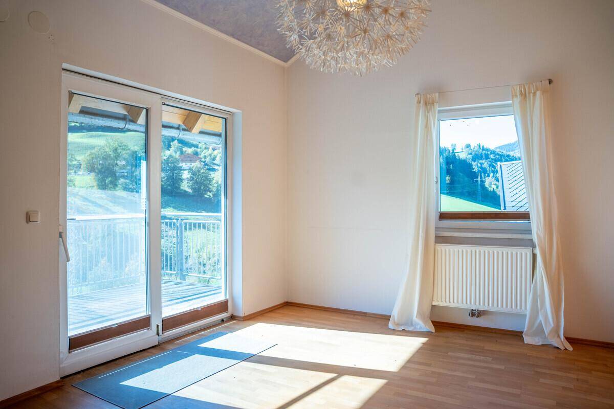 Schlafzimmer mit Holzboden, Zugang zum Balkon und Blick auf die grüne Landschaft.