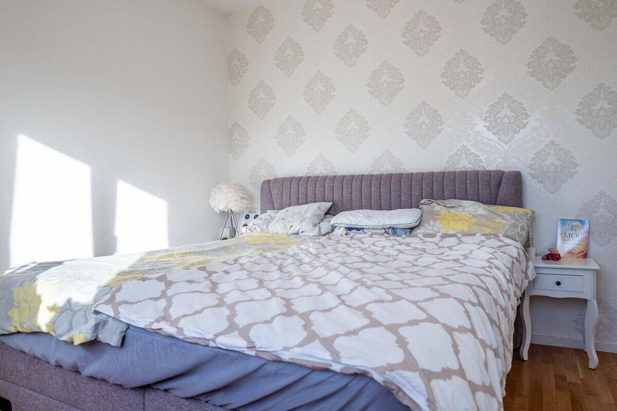 Helles Schlafzimmer mit gemusterter Tapete, großem Bett und Nachttisch.