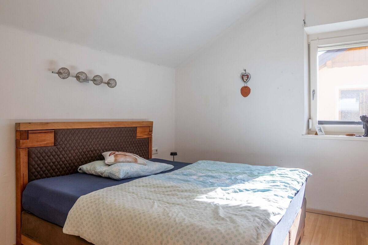 Schlafzimmer mit Holzbettrahmen, weiß gestrichenen Wänden und Fenster.