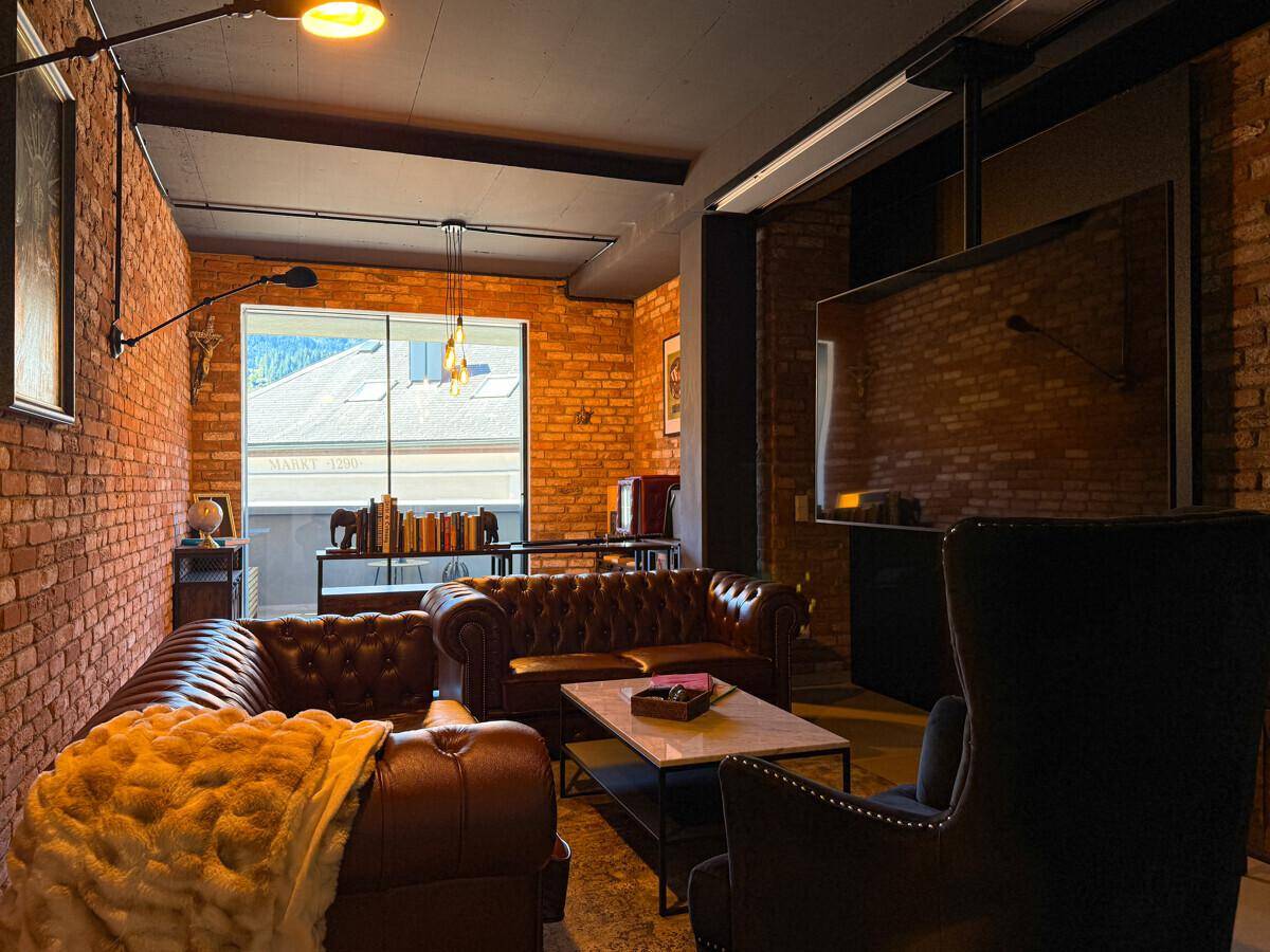 Stilvolles Wohnzimmer mit Chesterfield-Sofas, Ziegelwänden und großem Fernseher.