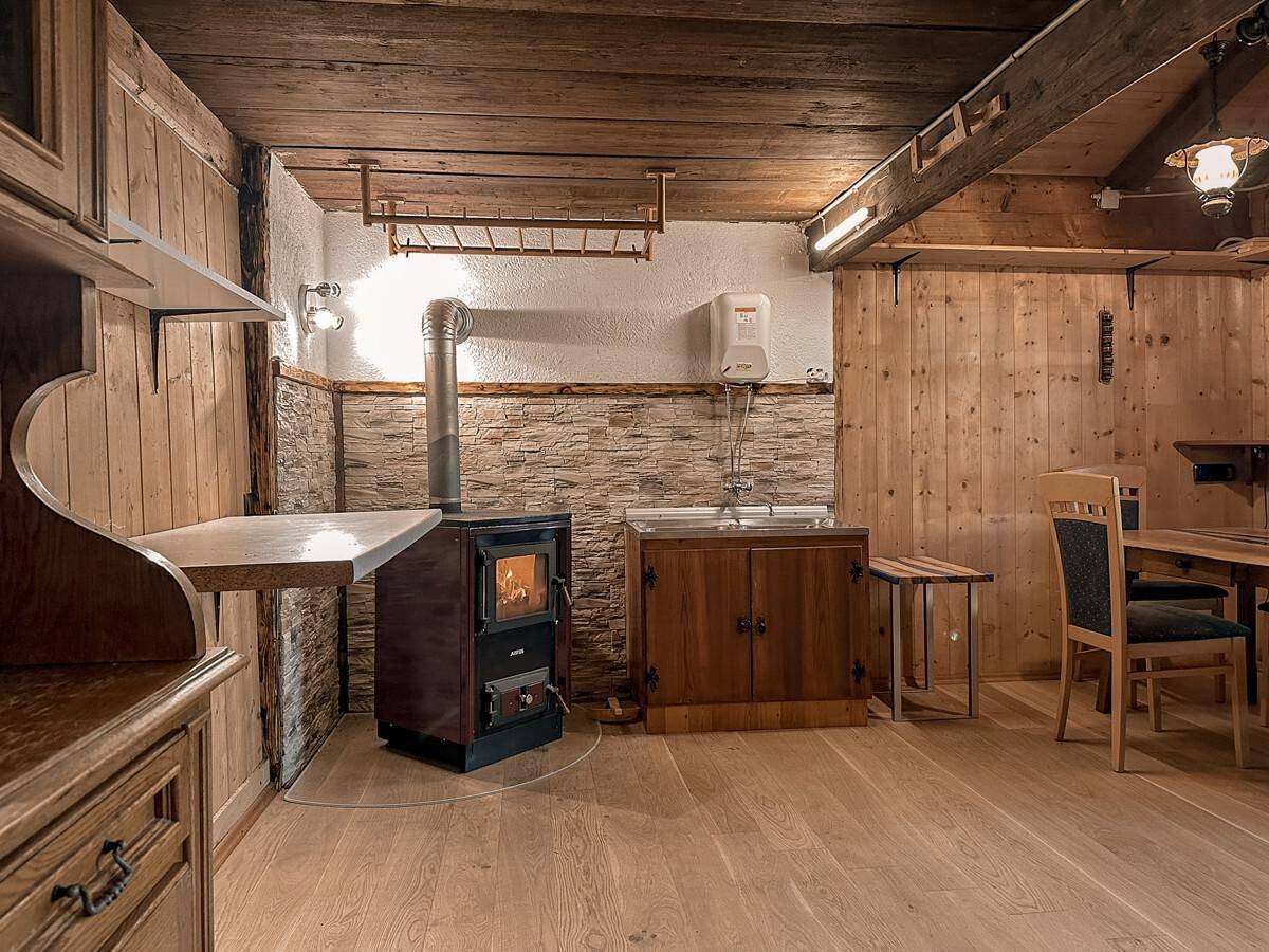 Rustikaler Raum mit Holzboden, Holzofen und einfacher Küchenzeile, ideal für gemütliche Abende im Chalet.